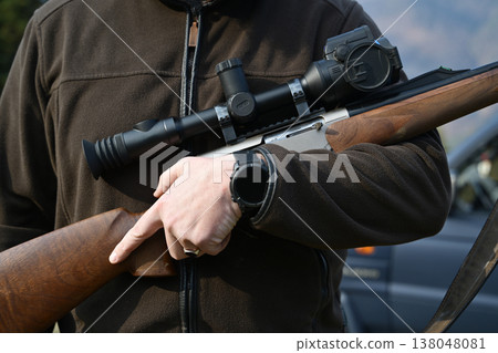 Hunter holding a scoped hunting rifle against his chest preparing for an outdoor hunt Hunter holding a scoped hunting rifle against his chest preparing for an outdoor hunt 138048081