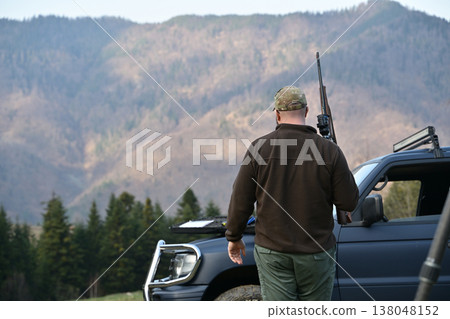 Hunter with rifle walking to pickup truck in mountain landscape during autumn hunting trip Hunter with rifle walking to pickup truck in mountain landscape during autumn hunting trip 138048152