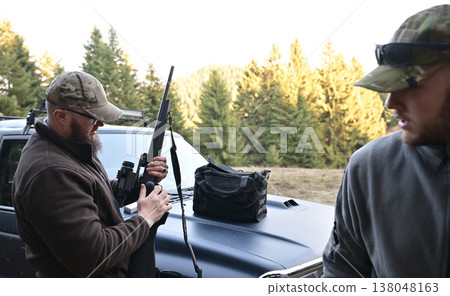 Two men preparing a rifle on a pickup truck before a hunt in a forest clearing 138048163