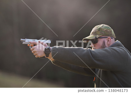 Man aiming handgun at outdoor shooting range wearing camouflage cap and sunglasses for tactical training Man aiming handgun at outdoor shooting range wearing camouflage cap and sunglasses for tactical training 138048173