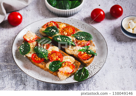 Baked bruschetta with caprese salad and spinach on a plate on the table 138049146
