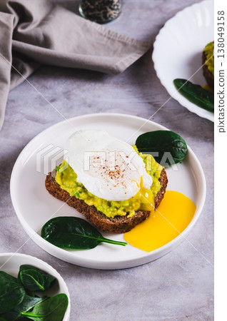Avocado sandwich with poached egg and spinach on a plate on the table vertical view 138049158