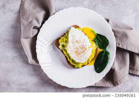 Close up of rye bread with guacamole and poached egg on a plate on the table top view Close up of rye bread with guacamole and poached egg on a plate on the table top view 138049161