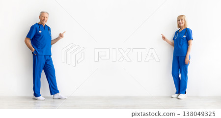 Senior male and female doctors pointing toward blank studio space between them Senior male and female doctors pointing toward blank studio space between them 138049325