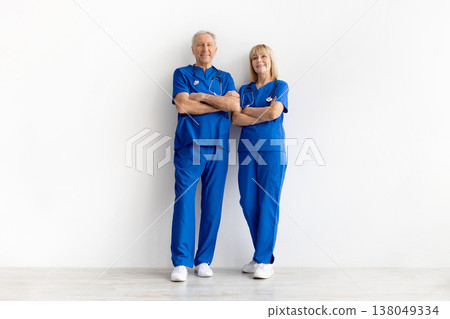 Mature male and female doctors wearing blue scrubs standing with arms crossed Mature male and female doctors wearing blue scrubs standing with arms crossed 138049334
