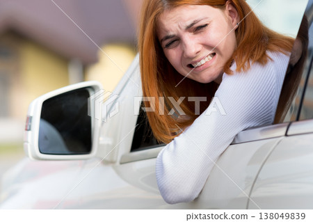 Young woman driving a car backwards. Girl with funny expression on her face while she made a fender bender damage to a rear vehicle. Young woman driving a car backwards. Girl with funny expression on her face while she made a fender bender damage to a rear vehicle. 138049839