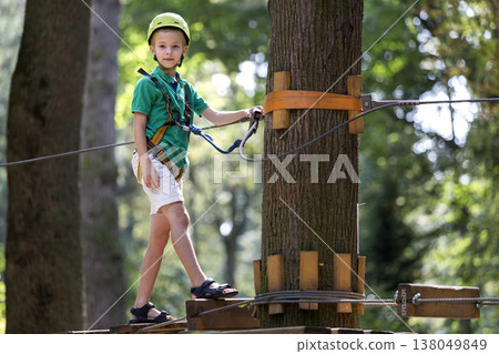 Young child boy in safety harness and helmet attached with carbine to cable on rope way in park. 138049849