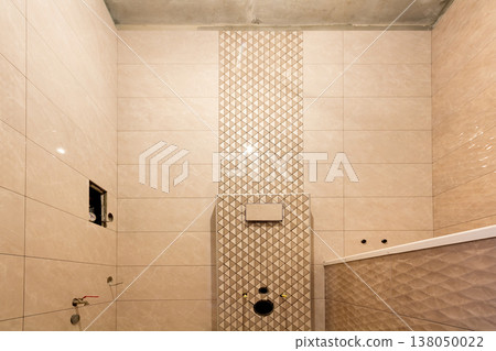 Unfinished reconstruction of bathroom or toilet with light beige geometric ceramic tiles installed on walls, place for lavatory and bath. Unfinished reconstruction of bathroom or toilet with light beige geometric ceramic tiles installed on walls, place for lavatory and bath. 138050022