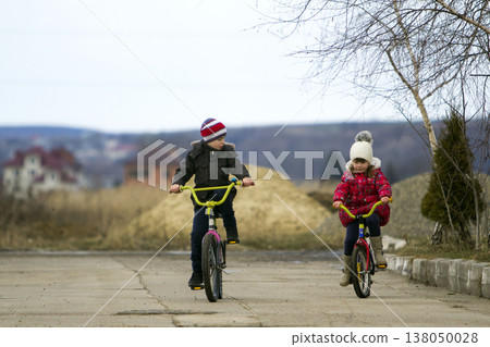 Two happy children boy and girl riding bicycles outdoors in cold weather Two happy children boy and girl riding bicycles outdoors in cold weather 138050028