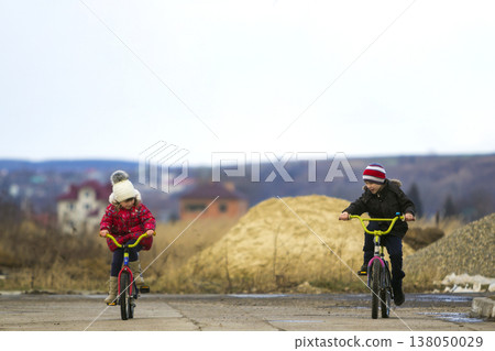 Two happy children boy and girl riding bicycles outdoors in cold weather Two happy children boy and girl riding bicycles outdoors in cold weather 138050029
