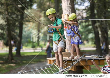 Two children, boy and girl in protective harness and safety helmets at climbing activity on rope way. 138050035