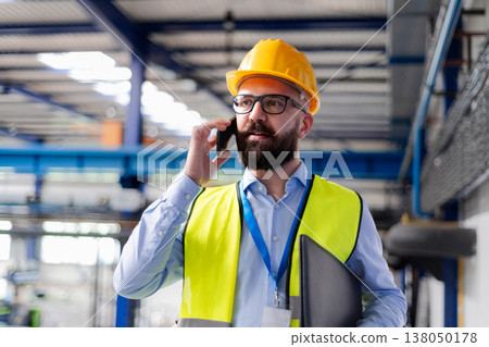Warehouse manager with safety helmet making phone call. Warehouse manager with safety helmet making phone call. 138050178