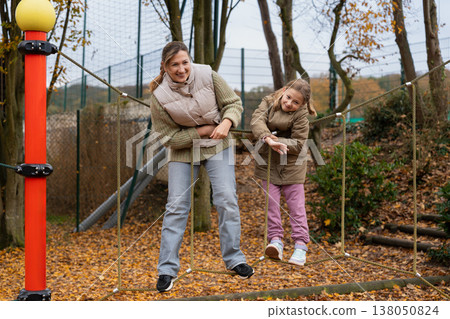 Mother balancing with daughter on rope bridge at playground autumn Mother balancing with daughter on rope bridge at playground autumn 138050824