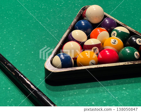 Billiard balls sit in a triangle on the green table, ready for players to start the game. Cue stick rests nearby Billiard balls sit in a triangle on the green table, ready for players to start the game. Cue stick rests nearby 138050847