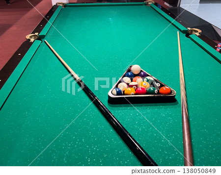 Billiard table is set up with a triangle of balls and cues positioned on either side for an upcoming game in a game room 138050849