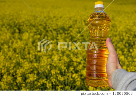 A man stands in a rapeseed field holding a clear bottle filled with rapeseed oil under the sun. The field is covered in yellow flowers A man stands in a rapeseed field holding a clear bottle filled with rapeseed oil under the sun. The field is covered in yellow flowers 138050863