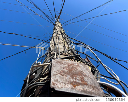 A tall electric pole stands upright with many wires extending from it against a clear blue sky. This scene shows the structure providing energy A tall electric pole stands upright with many wires extending from it against a clear blue sky. This scene shows the structure providing energy 138050864