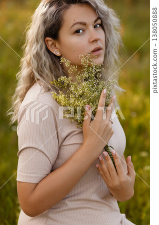 Young woman holding yellow wildflowers in meadow at golden hour, look at camera Young woman holding yellow wildflowers in meadow at golden hour, look at camera 138050888