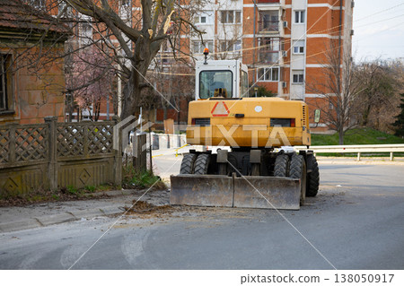Road maintenance vehicle parked on urban street near residential buildings and sidewalk. Infrastructure repair, municipal service work, traffic disruption and city maintenance activity Road maintenance vehicle parked on urban street near residential buildings and sidewalk. Infrastructure repair, municipal service work, traffic disruption and city maintenance activity 138050917