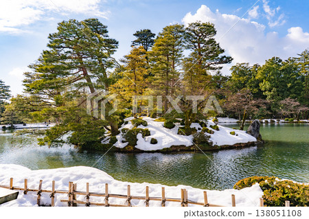 一幅美麗的日式庭園景色，展現了兼六園霞池中漂浮的蓬萊島，周圍環繞著皚皚白雪。 138051108