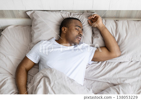 Young black man sleeping peacefully in bed during daytime, relaxed posture 138053229