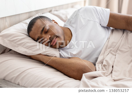 Handsome young black man sleeping peacefully on bed under blanket Handsome young black man sleeping peacefully on bed under blanket 138053257