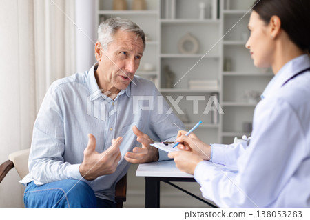 Senior male patient explaining symptoms to female doctor during clinic consultation 138053283