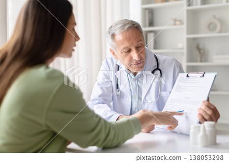 Senior male doctor explaining medical document and treatment plan to female patient 138053298