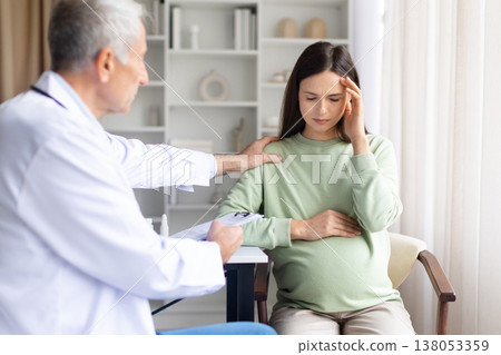 Pregnant woman suffering from headache during medical consultation while doctor provides support 138053359