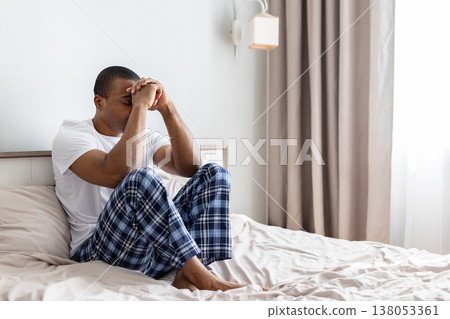 Young black man sitting on bed with hands clasped and head down Young black man sitting on bed with hands clasped and head down 138053361