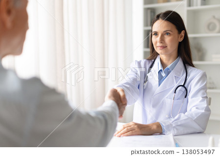 Female doctor shaking hands with male patient after successful consultation in clinic 138053497