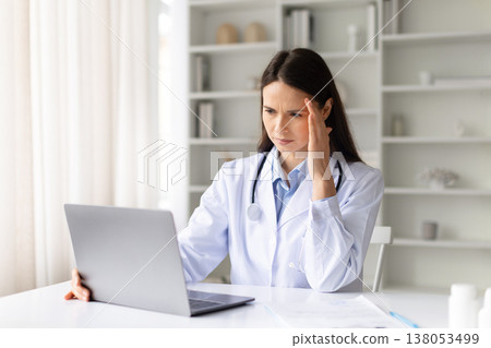 Stressed female doctor working on laptop in clinic office, touching her temple Stressed female doctor working on laptop in clinic office, touching her temple 138053499