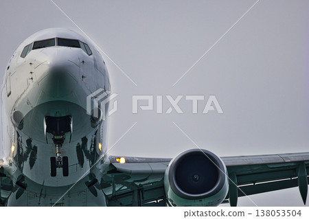 Low Angle Close-Up of a Commercial Passenger Airplane: Detailed View of the Aircraft Nose, Cockpit Windows, and a Jet Engine against a Grey Overcast Sky, Aviation and Travel Concept 138053504
