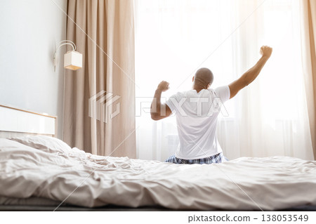 Young african american man stretching arms energetically on bed after waking up Young african american man stretching arms energetically on bed after waking up 138053549
