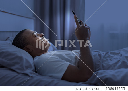 Young black man lying in bed at night using smartphone Young black man lying in bed at night using smartphone 138053555