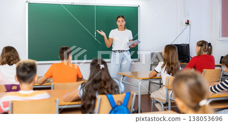 Woman teacher explaining new theme to children during class in primary school Woman teacher explaining new theme to children during class in primary school 138053696