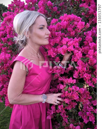 Woman in pink dress admires bright bougainvillea flowers 138053797