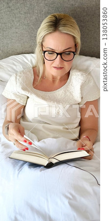 Relaxing with a book. Woman reading a book while lying in bed. Relaxing with a book. Woman reading a book while lying in bed. 138053860