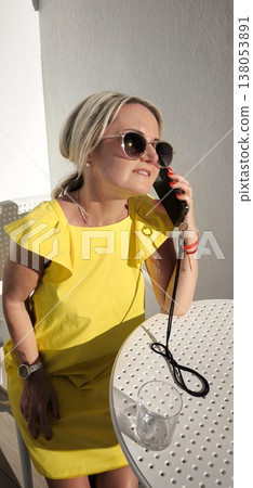 Blonde woman in yellow dress talking on phone outdoors 138053891