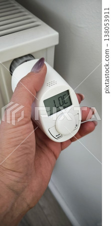 Smart thermostat: a woman's hand adjusts a modern thermostat on a heating radiator Smart thermostat: a woman's hand adjusts a modern thermostat on a heating radiator 138053911