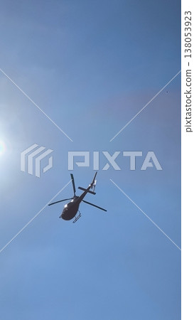 A bright red helicopter against a bright blue sky and sun 138053923