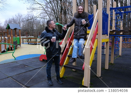 Father and daughter autumn playground colorful slide holding coffee cups dad helping girl descend steps cozy outdoor family moment Father and daughter autumn playground colorful slide holding coffee cups dad helping girl descend steps cozy outdoor family moment 138054036