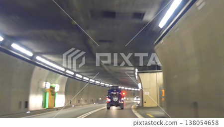 Car drives through a tunnel with lights and signs along the road in an urban area during the day Car drives through a tunnel with lights and signs along the road in an urban area during the day 138054658