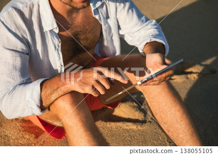 Man sitting on sand while looking at tablet in Bali Man sitting on sand while looking at tablet in Bali 138055105