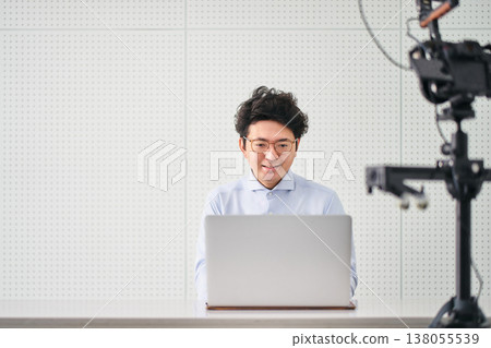 一位三十多歲、戴著眼鏡的男子正在操作電腦，同時進行視訊直播。 138055539