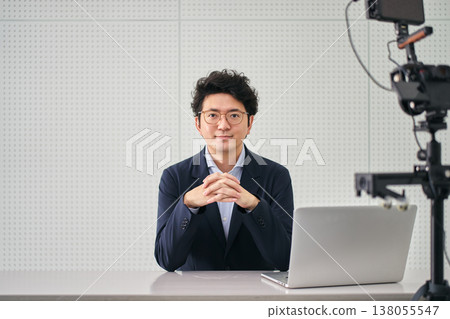 A male news anchor, looking directly at the camera, broadcasts news from a filming studio. 138055547