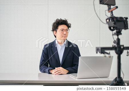 A male news anchor filming the news with a camera and computer in a filming studio. A male news anchor filming the news with a camera and computer in a filming studio. 138055549