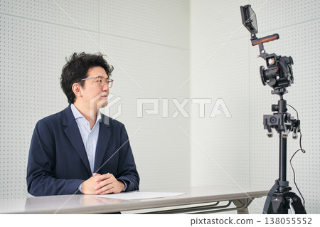 A news anchor reading a news script in front of the camera in a filming studio. A news anchor reading a news script in front of the camera in a filming studio. 138055552