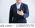 A man in a suit, faceless and facing forward, holding a smartphone, against a white background. 138055570