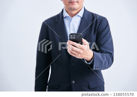 A man in a suit, faceless and facing forward, holding a smartphone, against a white background. A man in a suit, faceless and facing forward, holding a smartphone, against a white background. 138055570